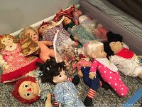Photo showing multiple vintage dolls including Raggedy Ann and Andy, Krissy, Drowsy, and others lying on the floor and couch