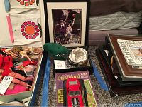 Wide view of the lot showing a box of dolls, signed Jets cap, mini Jets helmet, framed Jason Kidd and Shaquille O'Neal basketball photo, Disneyland puzzle and stacked picture frames.