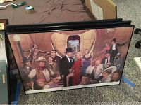 Wide view of three framed prints leaning against a piece of furniture, showing artwork and frames