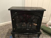 Image of the black electric space heater fireplace showing front closed door with curved glass, metal frame, and decorative grille.