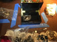 Full assortment of sterling silver jewelry displayed on a table, including chains, brooches, earrings, and the lacquer box with floral design.