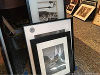 Three framed black and white photo prints leaning against a wall on carpet floor, showing parts of each photograph and black frames