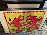 Keith Haring print with two dancing red figures and orange wavy border, framed behind acrylic