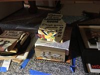 View of multiple wall art pieces arranged together including canvas floral prints stacked, wooden signs with various messages, and a metal rooster sign partially visible.