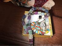 A box holding the necklace with acrylic cube beads in multi-colors, a pendant with turquoise and orange stones, and other small jewelry pieces.
