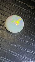 Round Ethiopian opal cabochon with multicolored play-of-color on dark surface