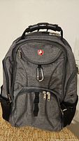 Front view of grey Swiss Gear backpack showing logo, compartments, carabiner, side pockets