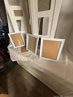 Three white 8×10 frames leaning against folded white room divider