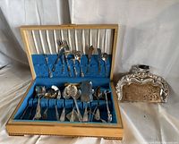 Open wooden chest with silver-plated flatware and separate ornate crumb tray