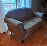 Front view of beige fabric loveseat showing rolled arms, nailhead trim and seat cushions