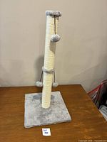 Full view of cat scratching tower showing base, post, and hanging pom balls