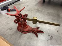 Full view of balance scale on floor showing red cast iron base, brass beam and weight