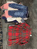 Stack of girls clothing showing plaid dress on top plus additional folded garments