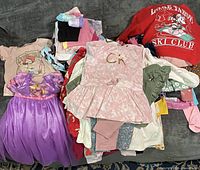 Pile of assorted girls toddler clothing showing variety of items including character tops, dress, sweatshirt, socks