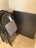 stacked four black metal folding chairs beside folded black table top