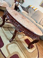 Oval coffee table angled view showing carved base and marble top