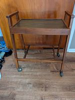 Full view of teak bar cart showing frame, tray, and casters