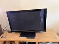 Front view of Panasonic plasma TV on stand with remote and cables visible