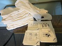 Stack of 11 linen tea towels beside 4 New Yorker cartoon cocktail napkins