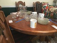 Close up of oak dining table top surface with assorted glassware and mugs (not included).