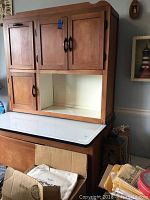 Front view of three-piece assembled cupboard showing upper hutch, open cubby (roll-down door missing), enamel tabletop