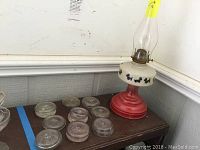 Red and white vintage oil lamp with glass chimney and Scottie dog silhouettes on white midsection, placed on a wooden surface.