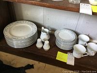 Full set of Sheffield Blue Whisper china pieces including stacked dinner plates, bread plates, cups, creamer, and salt and pepper shakers on a wooden shelf.