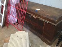 Side view of the heavily used cedar chest with damaged finish and miscellaneous items partially visible inside.