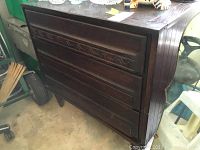 Side view of the three drawer wooden chest showing carved drawer fronts and legs.