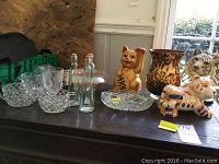 Lot displayed on wooden table with cut glass creamers, sugar dish, candy dishes, glass bottles, animal figurines including cat and tigers, and leopard print vase.