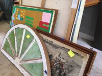 Image shows the half moon window frame with green tinted glass leaning against several framed artworks with visible distressed wood and chipped paint.