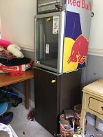 Red Bull mini refrigerator with glass door and neon light on top of GE mini refrigerator with dark wood exterior.