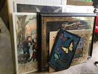 Stack of six framed wall art pieces including children, animals, and advertising prints
