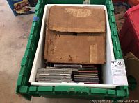 Green bin containing heavily worn sleeves housing vintage 78 rpm records, along with a collection of CDs and DVDs below in plastic container.