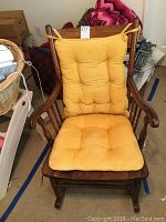 Front view of traditional wooden rocking chair with yellow padded seat and back cushions tied on.