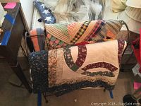 Photo showing two handmade quilts draped over metal rack with visible patchwork and applique patterns.