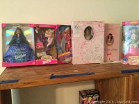 Collection of six Barbie dolls in original boxes displayed on a wooden surface showing variety of dolls