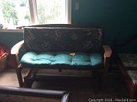 Full view of solid wood glider with floral back cushion and teal seat cushion, against a window.