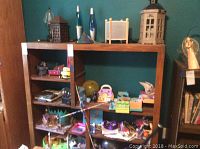 Photo showing a variety of items on a wooden shelf including toys, lamps, miniature furniture, and decor pieces.