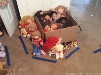Wide angle showing multiple large Cabbage Patch dolls inside a cardboard box and some on the floor around it