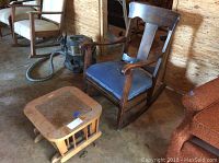 Wooden rocking chair with blue upholstered seat and wooden glider foot stool placed on a concrete floor in a storage area.