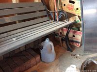 Side view showing wooden slats for seat and backrest and ornate metal armrest with decorative scrollwork.