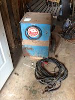 Front view of blue Hobart welding unit with attached cables and clamps on the floor.