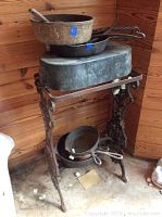 View of the cast iron pots, skillets, and stand showing several pots stacked on and under the stand in a corner with wooden wall paneling.