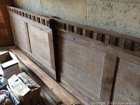 Photo showing three long wooden panels with decorative dentil molding on top, placed against a wall with some boxes and glass jars in front.