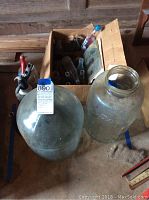Photo showing large clear glass jug bottles and a box containing more glass bottles.
