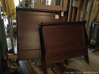 Side view of wooden headboard and footboard standing upright in basement with dust and storage items visible