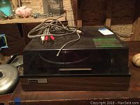 Front angled view of Panasonic turntable powered off, sitting on wooden surface with cables on top.