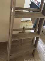 Close-up side view of wooden step ladder showing three slatted steps and horizontal braces.