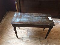 Photo of rectangular wooden piano bench top showing surface wear and nicks.